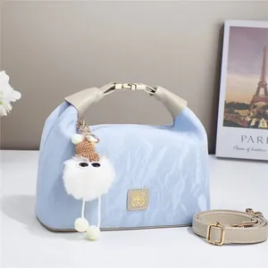 Detail of light blue textured handbag with plush charm and elegant gold metal lock