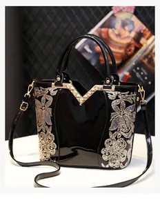 Detail of black patent leather bag featuring floral embroidery and V-shaped metal trim