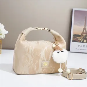 Elegant beige textured handbag with plush charm and gold hardware on white surface