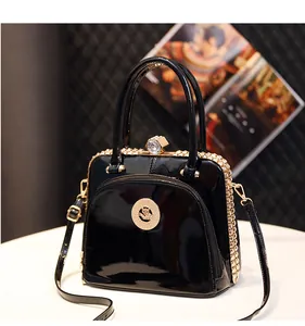 Detail einer schwarzen Lacklederhandtasche mit Goldemblem und sechseckigem Kristallverschluss