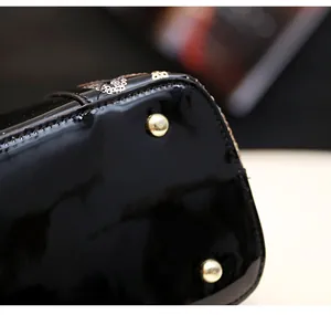 Detailed close-up of glossy black leather bag bottom with protective gold metal studs