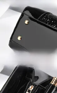 Detail of glossy black patent leather handbag with gold rivets and metallic zipper