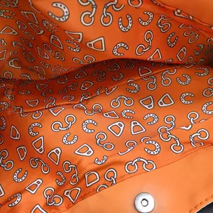 Detail of orange canvas bag lining with equestrian print and magnetic buckle closure