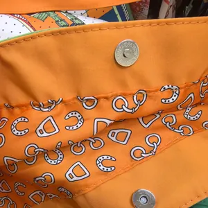 Detailed macro view of orange canvas bag featuring magnetic buckle and equestrian lining