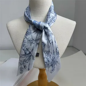 Detail of bamboo and bird print on light blue narrow polyester scarf tied on mannequin