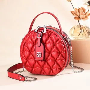 Detail of red quilted round crossbody bag with silver clover charm and chain strap
