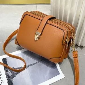 Detail van een bruine crossbodytas van zacht leer met gouden ritsen en hardware
