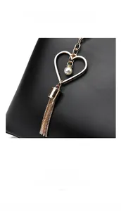 Dettaglio del pendente a cuore dorato con perla e nappe a catena su borsa in pelle martellata nera