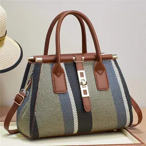 Détail du sac cabas jacquard rayé avec sangles en cuir et boucle dorée sur un mur beige