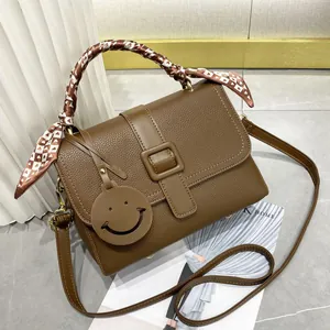 Détail du sac à main en cuir marron grainé avec foulard à motifs cœurs et charm sourire