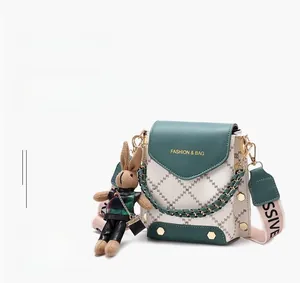 Detail of green and white crossbody bag with metal studs, wide strap, and rabbit charm