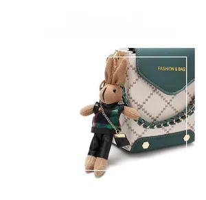 Detailed view of a knitted bunny bag charm with a plaid scarf on a leather handbag