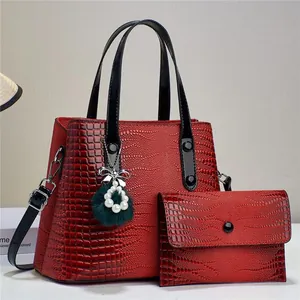 Detailed view of red crocodile pattern handbag with pearl bow pendant and fur ball accessory