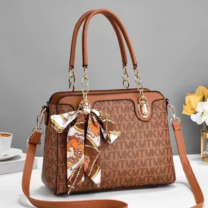 Detail der braunen Handtasche mit Logo-Muster, goldenen Ketten und dekorativem Seidenschal