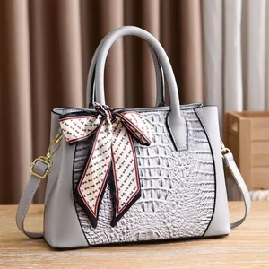 Detail of grey crocodile embossed handbag with elegant silk scarf and gold hardware
