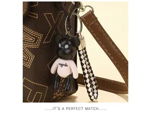 Close-up of brown patterned leather bag with a bear doll charm and woven lanyard
