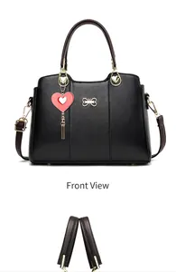 Close-up of black leather handbag featuring golden bow and red heart pendant detail