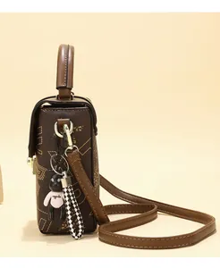 Detail view of mini crossbody bag in dark brown with geometric print and bear charm