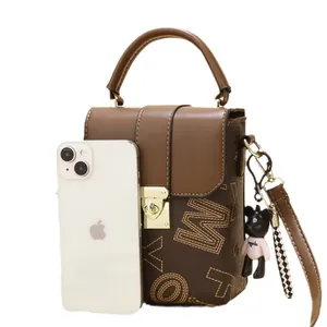 Brown vintage mini crossbody bag with letter print and bear charm next to a phone