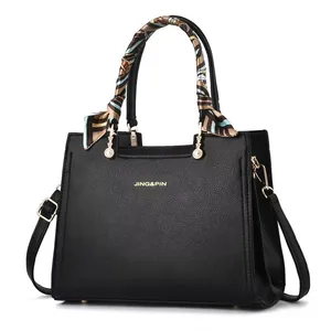Dettaglio borsa nera in pelle martellata con finiture dorate e foulard di seta