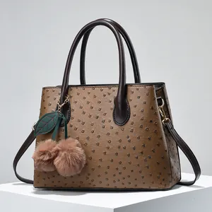 Brown ostrich texture handbag with gold hardware and plush cherry charm on white pedestal