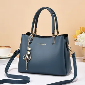 Detail of dark blue leather handbag with gold logo, heart charm and pearl accessory