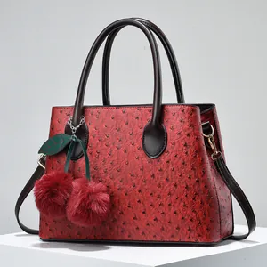 Macro shot of red ostrich texture handbag with cherry plush charm and golden metal hardware