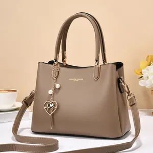 Close-up of taupe leather tote with golden lettering and elegant pearl heart pendant charm