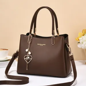 Detail of brown leather handbag with gold lettering, pearl heart charm and strap