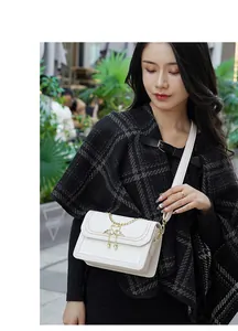 Détail du sac bandoulière en cuir blanc avec boucle cygne dorée sur fond à carreaux