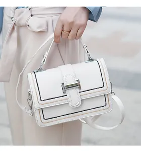Close-up of a white leather crossbody bag featuring silver metal lock and stitched detail