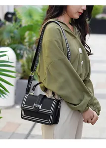 Detailed view of a black crossbody bag with white stitching and H-shaped silver buckle