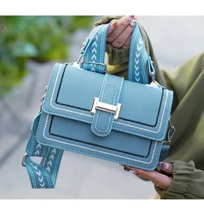 Close-up of light blue leather crossbody bag with silver buckle and wide geometric strap