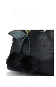 Close-up of black lychee leather handbag with decorative fur ball and leaf charms