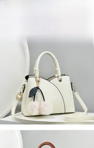 Detail of white litchi pattern leather handbag featuring a cute pink cherry pom pom charm