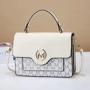 Close-up of cream white handbag featuring golden M logo and monogram pattern detailing