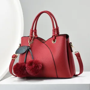 Deep red leather crossbody handbag with cherry charm on a white minimalist pedestal