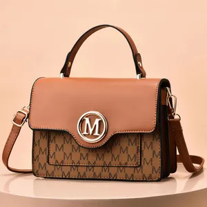 Close-up of caramel brown handbag with letter M monogram pattern and gold metal logo