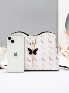 Sac à bandoulière crème avec motif cerf et pendentif papillon à côté d'un smartphone