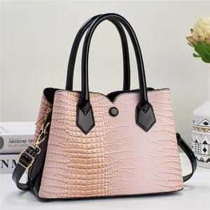Detail of pink crocodile embossed leather tote bag with black handles and metal buckles