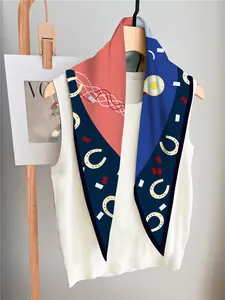 Detail of silk-feel scarf with horsebit pattern draped on wooden hanger and knit top