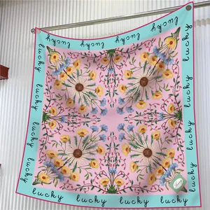 Pink daisy floral silk scarf with lucky lettering and light blue border hanging on a rod