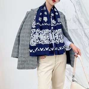 Detail van een marineblauwe sjaal met witte barokpatronen over een grijze blazer