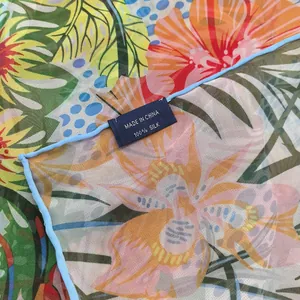 Detailed macro view of 100% silk scarf with tropical floral print and blue hand-rolled edge