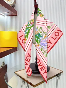 Dettaglio di un foulard in seta rosa con scritta LOVE e stampa di gigli su un manichino