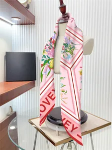 Dettaglio di un foulard in seta rosa con stampa a gigli e testo LOVE su un manichino