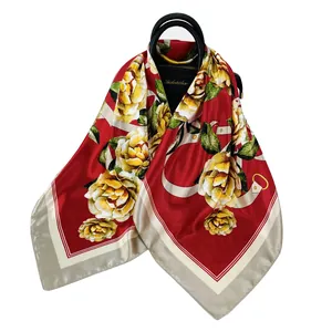 Dettaglio della sciarpa di seta rossa con fiori e catene legata a una borsa nera