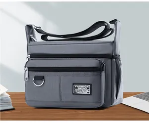 Close-up of grey waterproof oxford crossbody bag with multiple zipper pockets on wood desk