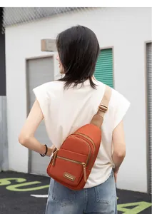 Detailed outdoor view of a brick-red nylon crossbody bag with three zipper compartments