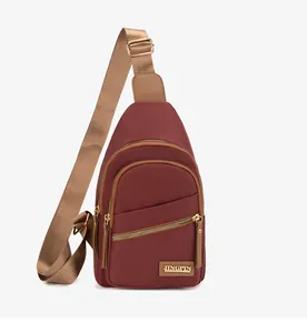 Detail of burgundy nylon chest bag with golden zippers and adjustable brown strap